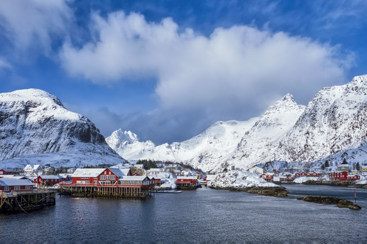 Å Rorbuer i vintersol med snødekte fjell i bakgrunnen.